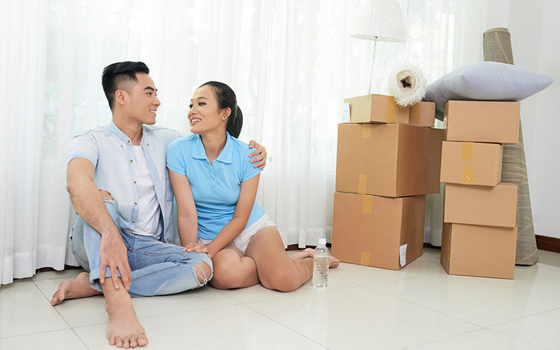 Smiling couple sitting on the floor surrounded by cardboard boxes, taking a break while moving into a new home