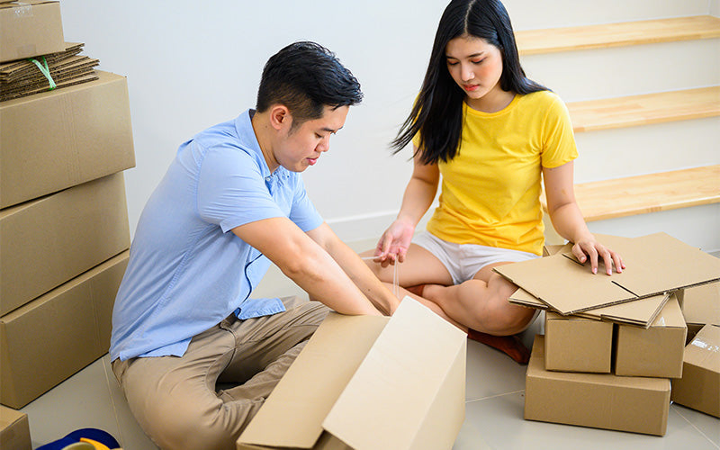 Young couple sitting on the floor assembling cardboard boxes together while preparing for a move